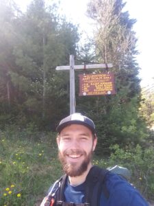 Chase Gregory poses for a selfie in front of a Finger Lakes Trail Sign