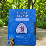 Close up photo of the blue Lewis and Clark Junior Ranger booklet with a Junior Ranger badge propped in front of it.