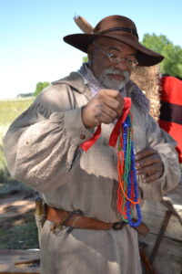 A man with a beard and glasses in period garb shoews off a strand of colorful beads