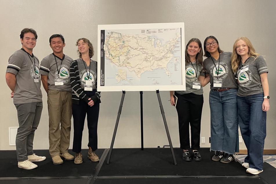 6 Trail Apprentices stand next to a National Trails System map on a presentation stage