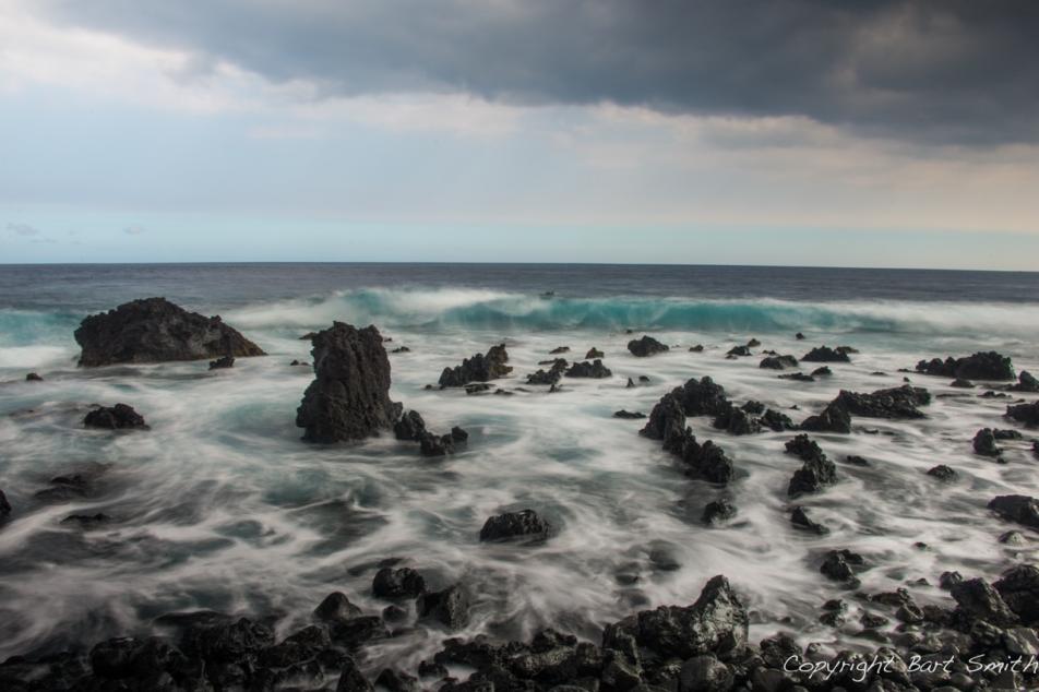 Ocean waves crashing over black rocks