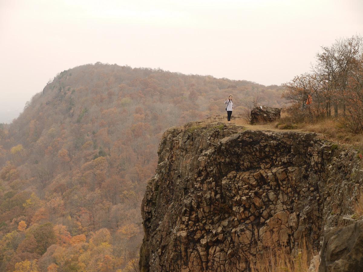 Cliff with a person looking towards a mountain in the distance during autumn
